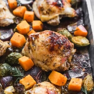 Baked honey mustard chicken thighs on a sheet pan with red onion, butternut squash, and brussels sprouts.