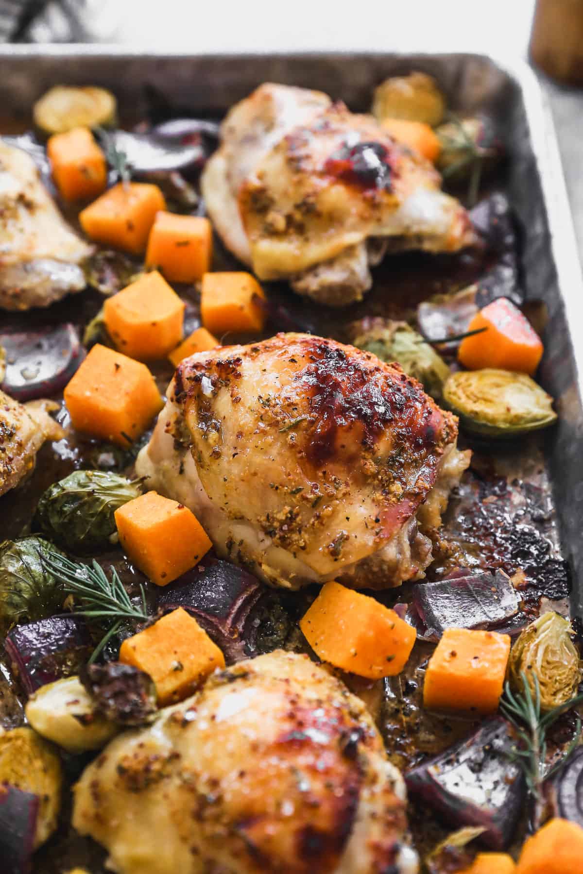 Baked honey mustard chicken thighs on a sheet pan with red onion, butternut squash, and brussels sprouts. 