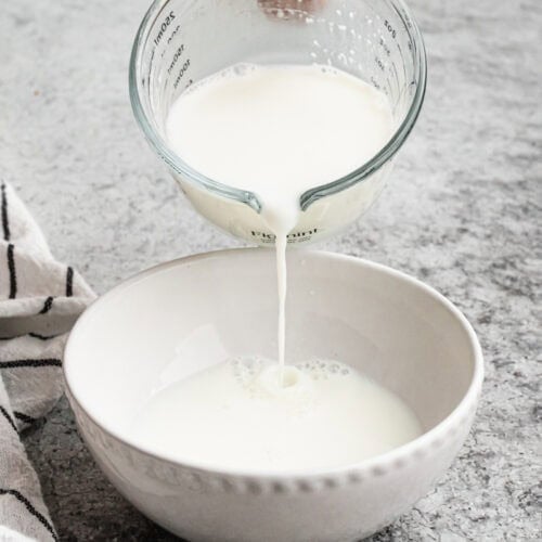 An easy buttermilk alternative being poured from a liquid measuring cup to a white bowl to use in a recipe.