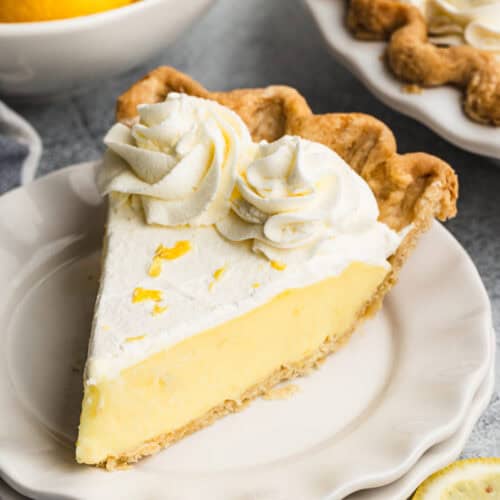 A slice of Sour Cream Lemon Pie, topped with sweetened whipped cream and lemon zest, ready to enjoy.