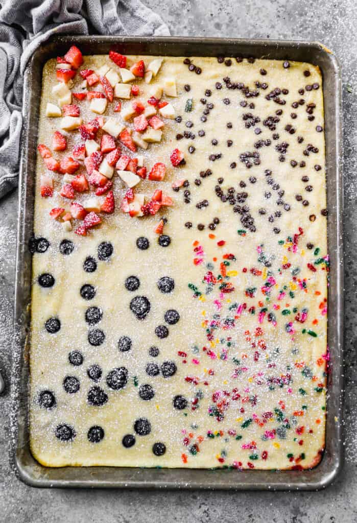 Easy Sheet Pan Pancakes divided into four quarters of flavors: sprinkles, blueberries, mini chocolate chips, and fresh strawberries and bananas.