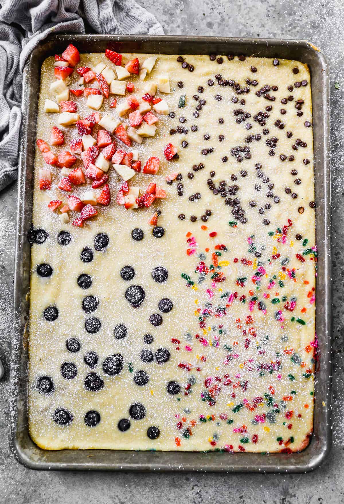 Easy Sheet Pan Pancakes divided into four quarters of flavors: sprinkles, blueberries, mini chocolate chips, and fresh strawberries and bananas. 