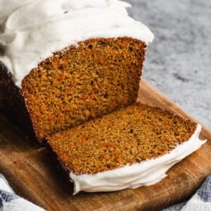 A Carrot Cake Loaf topped with cream cheese frosting, with one piece sliced to show the inside.