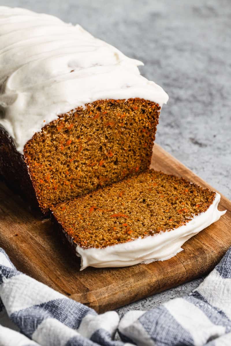 A Carrot Cake Loaf topped with cream cheese frosting, with one piece sliced to show the inside.