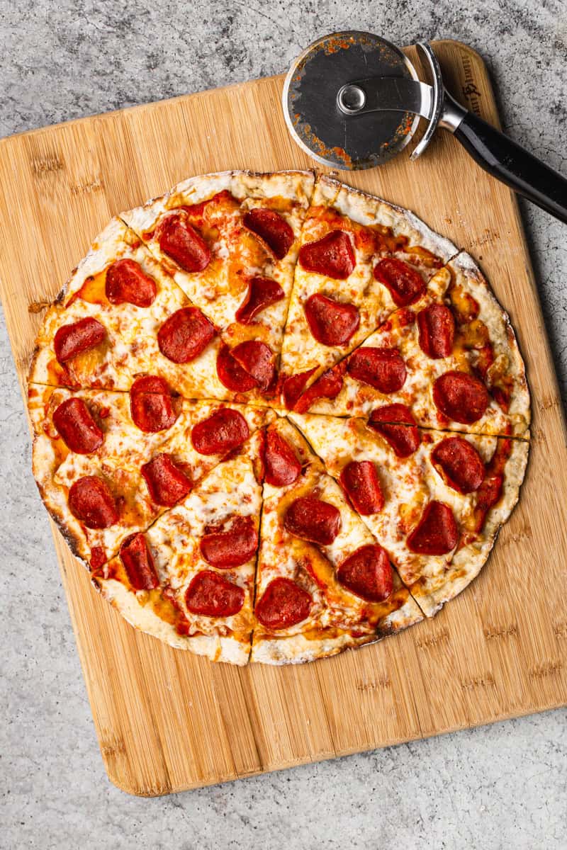 A protein pepperoni pizza on a cutting board, sliced and ready to serve. 