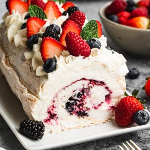 A meringue roulade dessert with a berry filling, topped with whipped mascarpone cream and fresh berries.