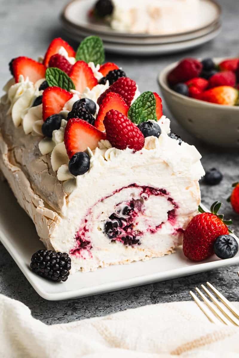 A meringue roulade dessert with a berry filling, topped with whipped mascarpone cream and fresh berries.