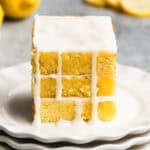 Three lemon brownies stacked on top of each other on a white plate with a simple glaze dripping down the sides.