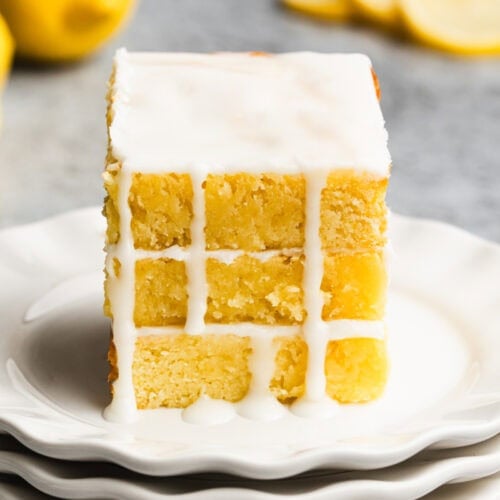 Three lemon brownies stacked on top of each other on a white plate with a simple glaze dripping down the sides.