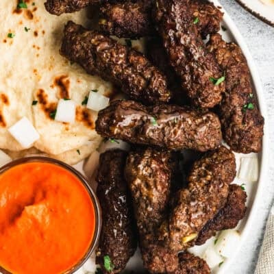 The best Cevapi recipe served on a plate with fresh pita bread, ajvar sauce, and sprinkled with chopped onion.