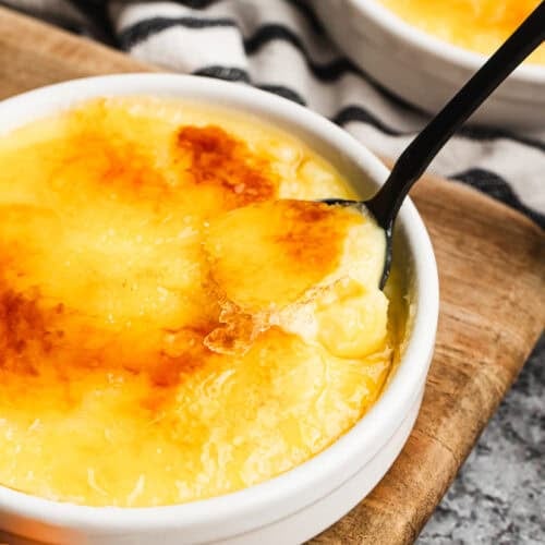 A Spanish Crema Catalana recipe in a shallow ramekin, topped with a layer of caramelized sugar being scooped up with a spoon.