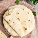 A stack of homemade flour tortillas on a clean kitchen cloth, ready to serve.