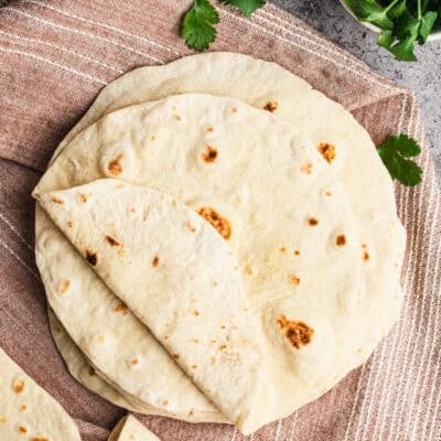 A stack of homemade flour tortillas on a clean kitchen cloth, ready to serve.