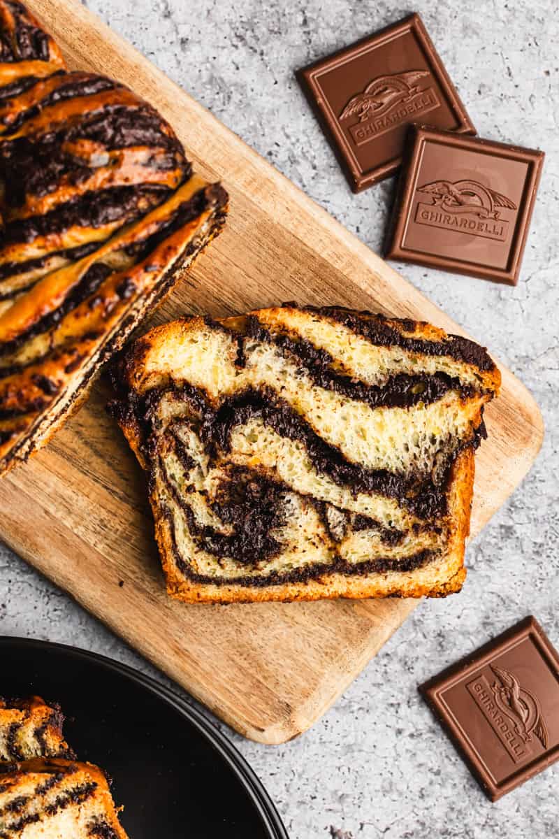 A slice of an easy Chocolate Babka recipe with chocolate swirls throughout on a cutting board.