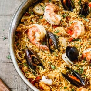 A pan of authentic Fideuà with clams, mussels, and shrimp nestled in the noodles, ready to serve.