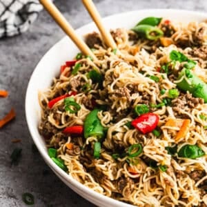 Beef Mongolian Noodles served in a bowl with chopsticks grabbing some noodles.