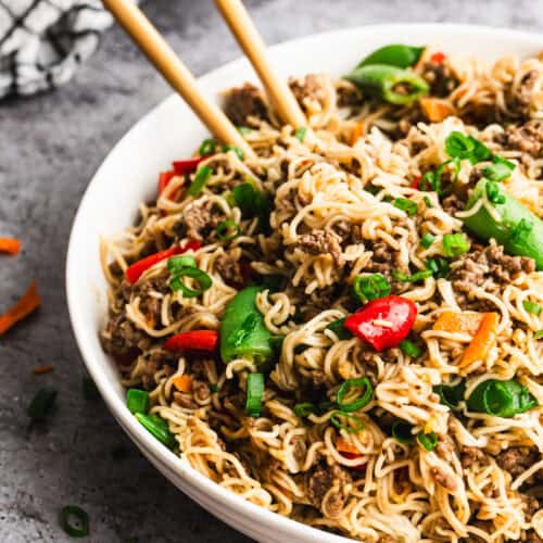 Beef Mongolian Noodles served in a bowl with chopsticks grabbing some noodles.