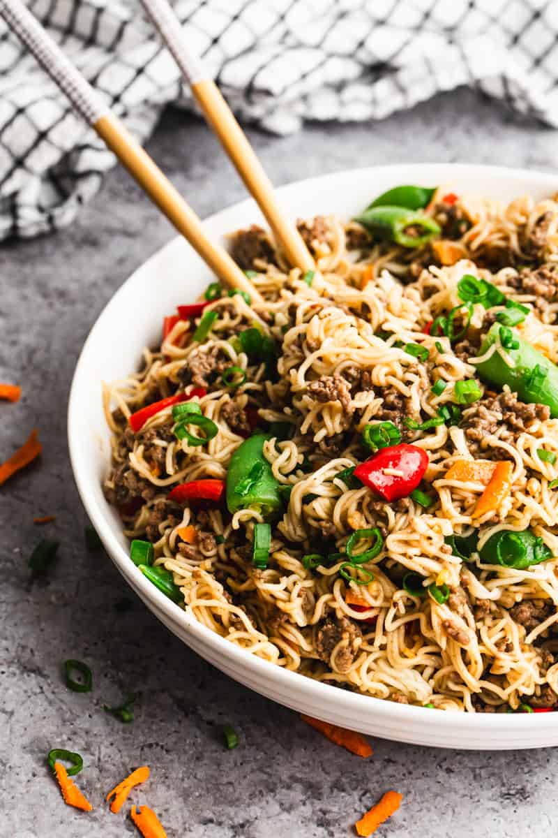 Beef Mongolian Noodles served in a bowl with chopsticks grabbing some noodles.
