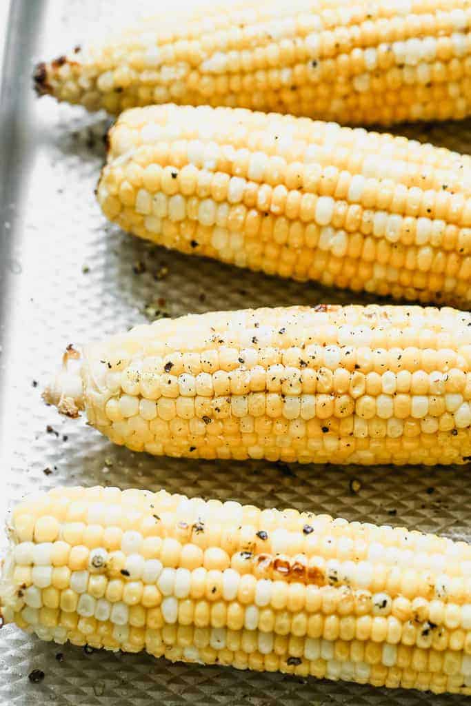 Grilled corn on the cob on a baking sheet dusted with salt and cracked pepper. Cooked to perfection and perfect ot use in salads, dips, or corn chowder.