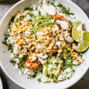 A Street Corn Chicken Rice Bowl with juicy chicken, creamy charred corn, and topped with avocado and a slice of lime with a creamy sauce drizzled on top.