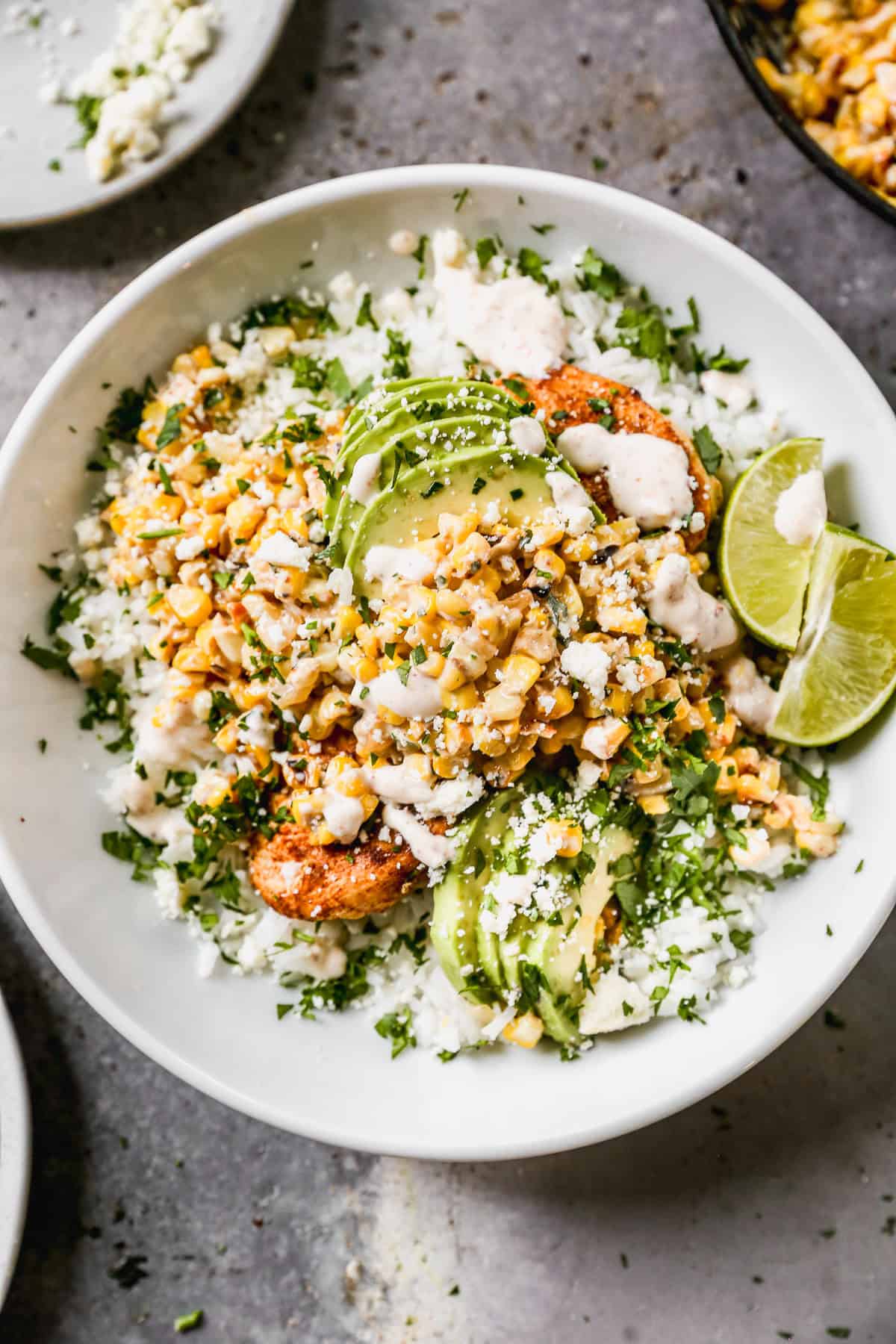 A Street Corn Chicken Rice Bowl with juicy chicken, creamy charred corn, and topped with avocado and a slice of lime with a creamy sauce drizzled on top.