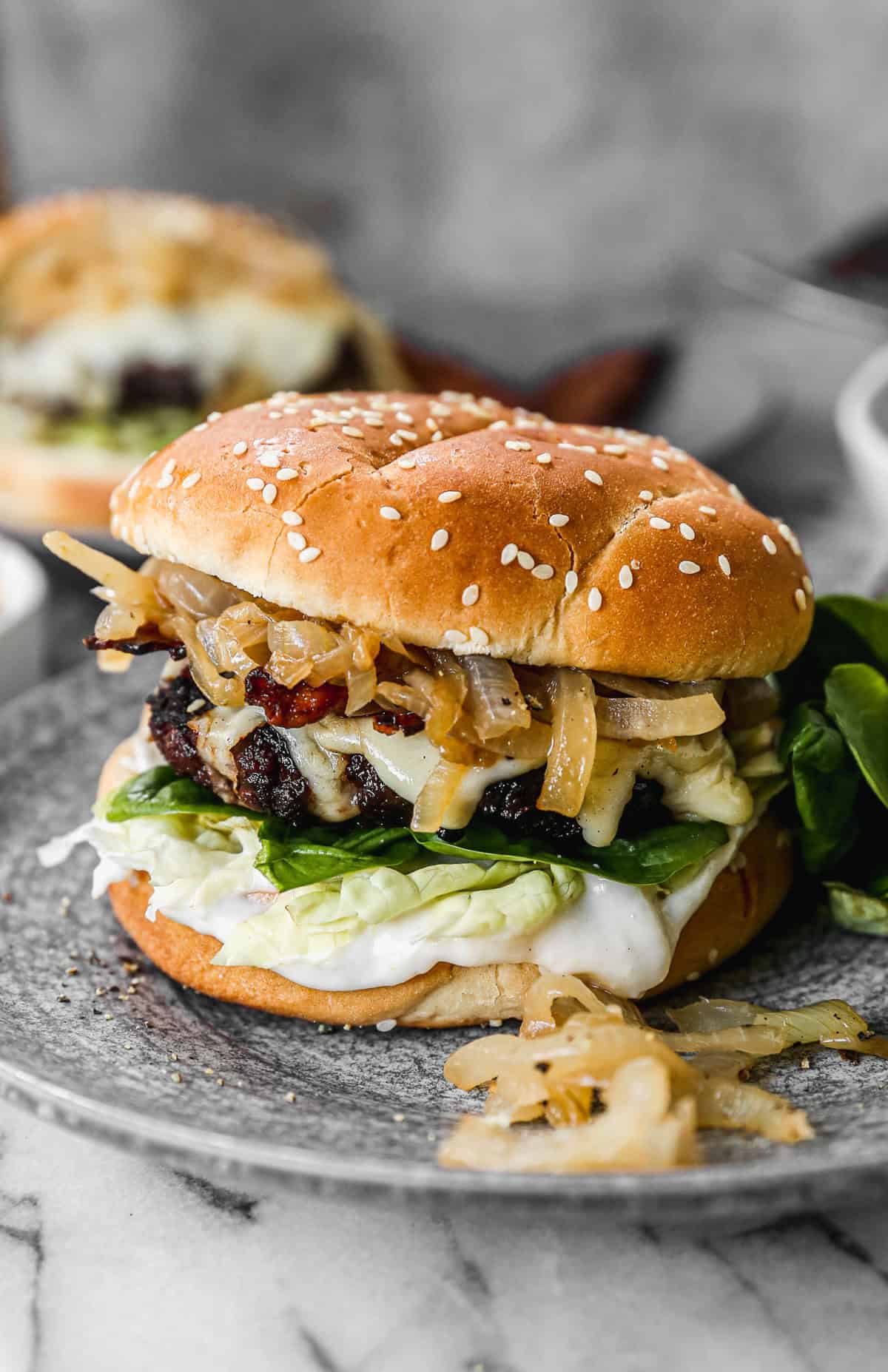 This French Onion Burger recipe includes a flavorful patty topped with caramelized onions, bacon, Gruyère cheese, arugula, and an easy horseradish aioli. I promise it will be your new favorite burger!