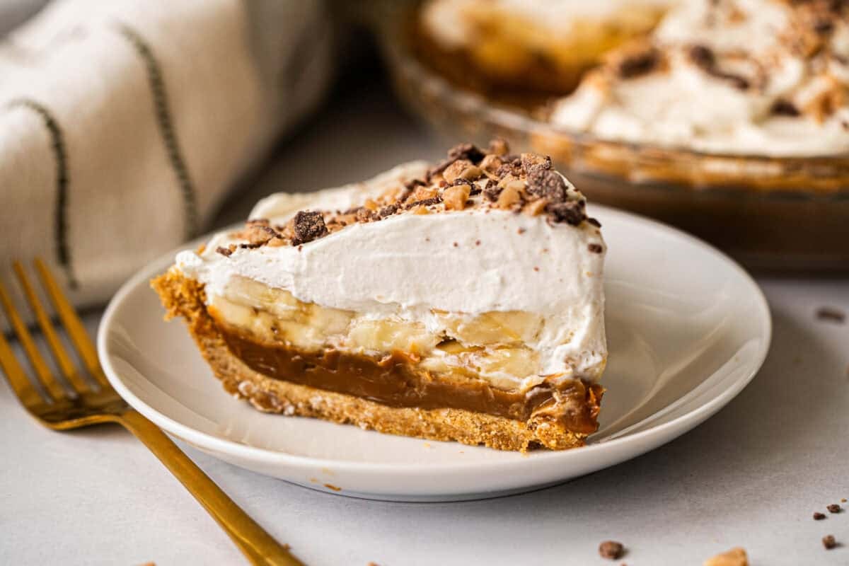 This easy Banoffee Pie recipe is simple to make but the flavors compliment each other perfectly with a graham cracker crust, dulce de leche, banana slices, and whipped cream with toffee bits on top.