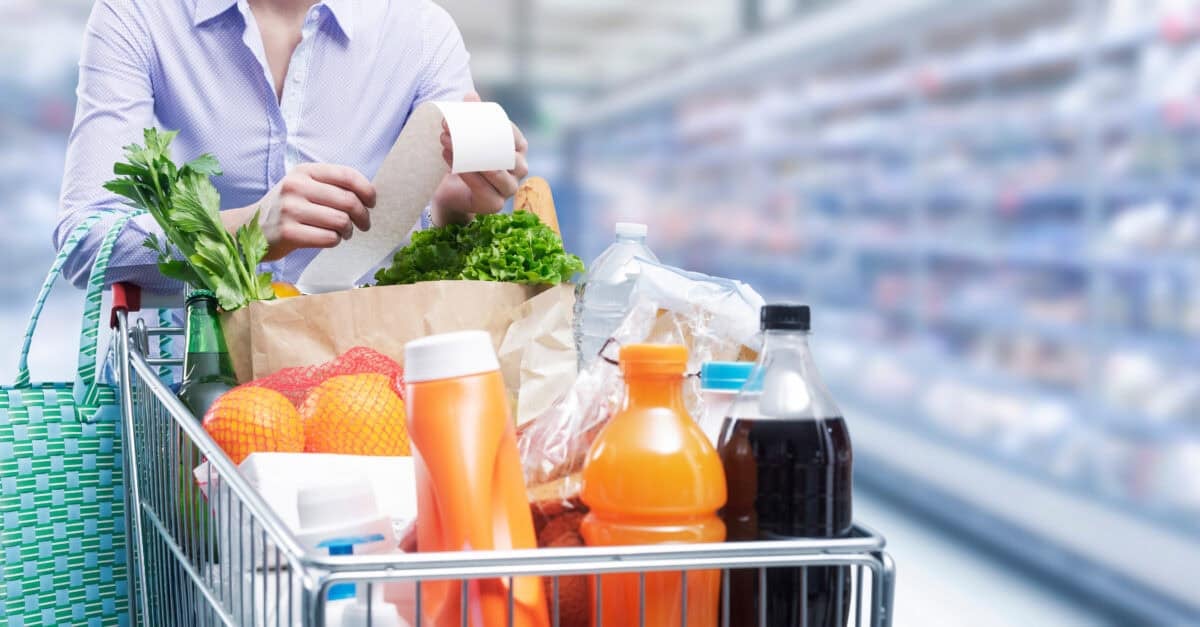 Woman pushing a cart and checking a grocery receipt, grocery shopping and expenses concept