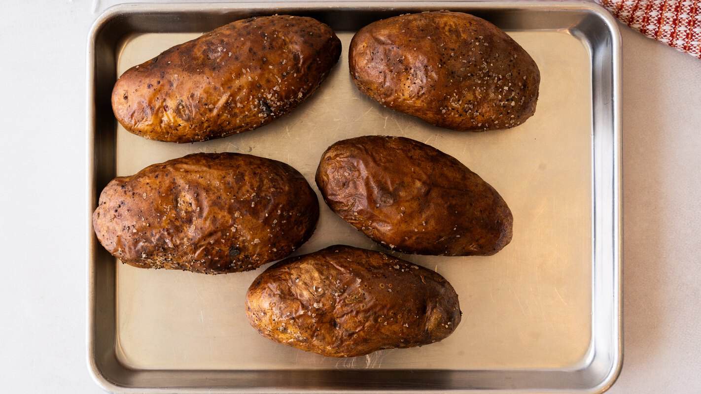 Five oven-baked russet potatoes on a baking sheet, ready to scoop for baked potato soup