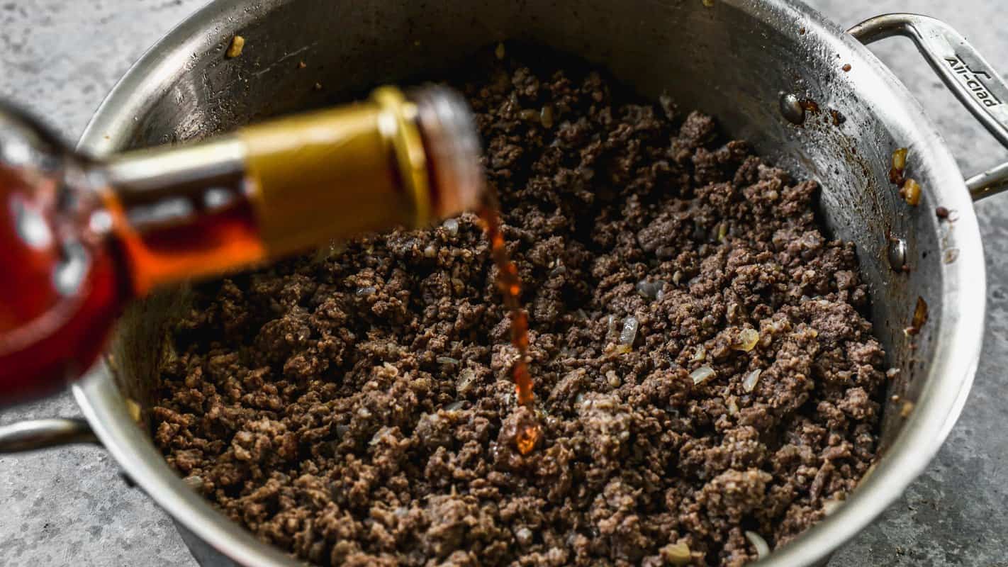 Red wine vinegar being poured over browned ground beef and sausage in a pot for homemade chili