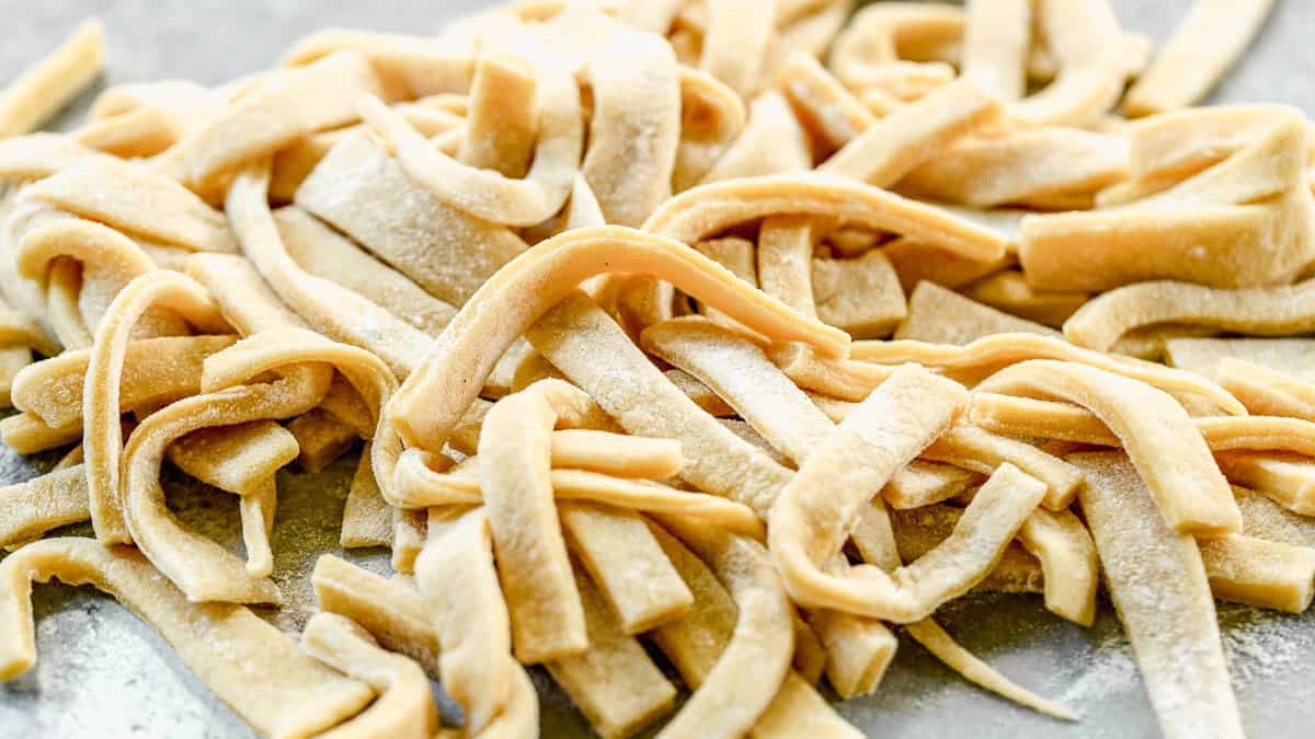 Freshly cut homemade egg noodles dusted with flour, ready to drop into chicken noodle soup
