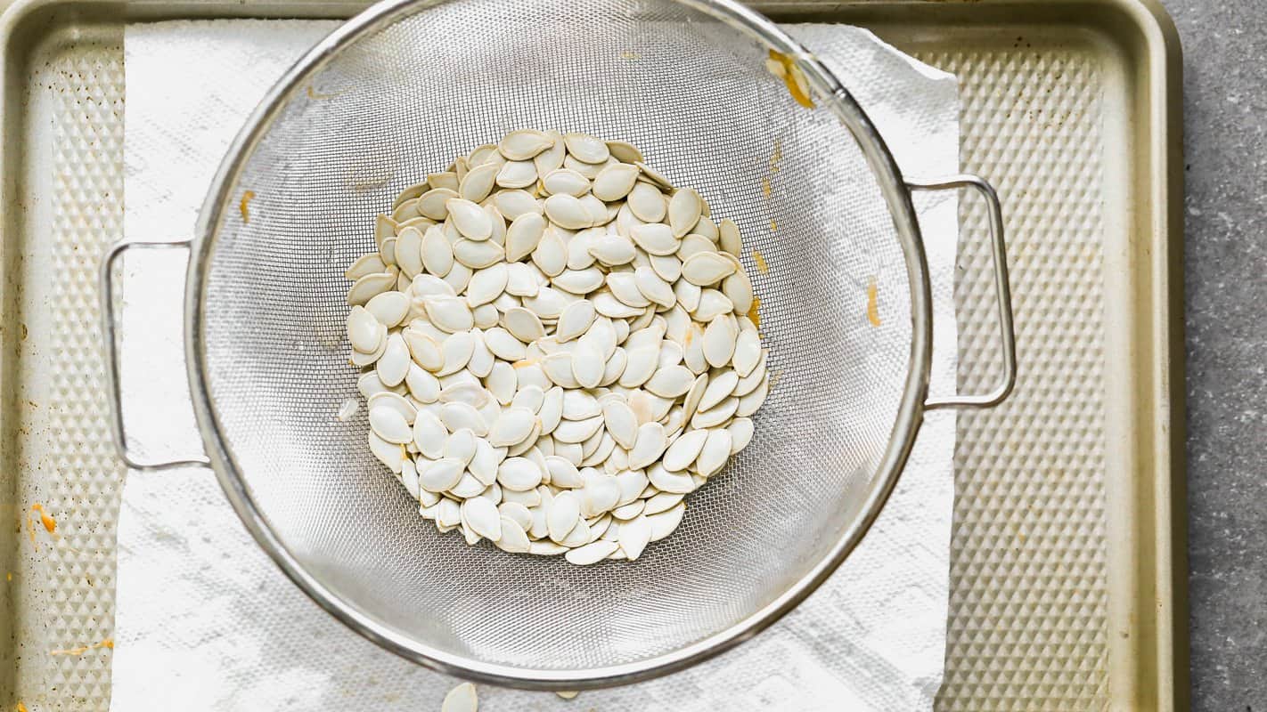 Cleaned pumpkin seeds in a mesh colander set over paper towels